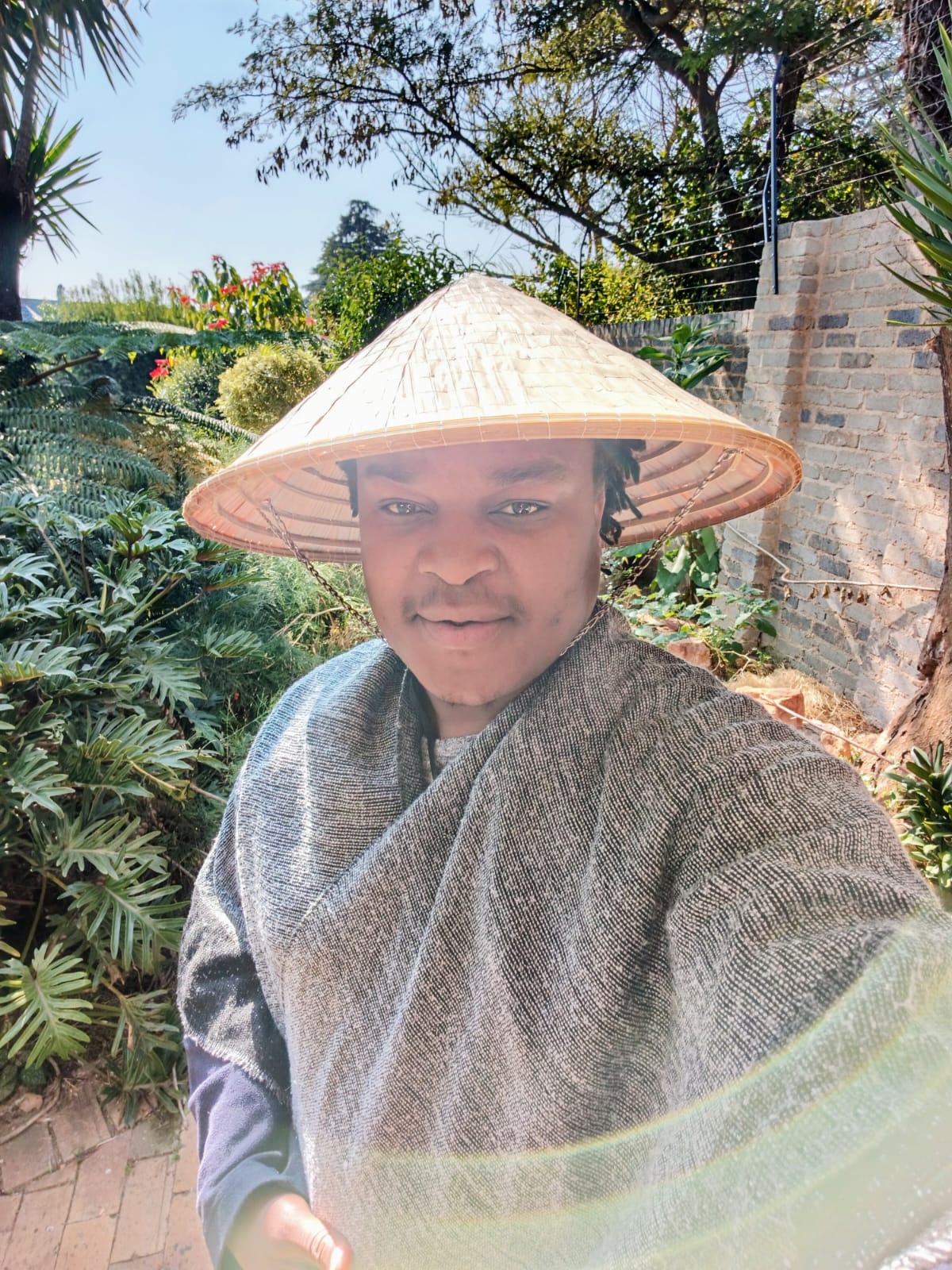 Anoshamisa in a lush garden, wearing a woven hat