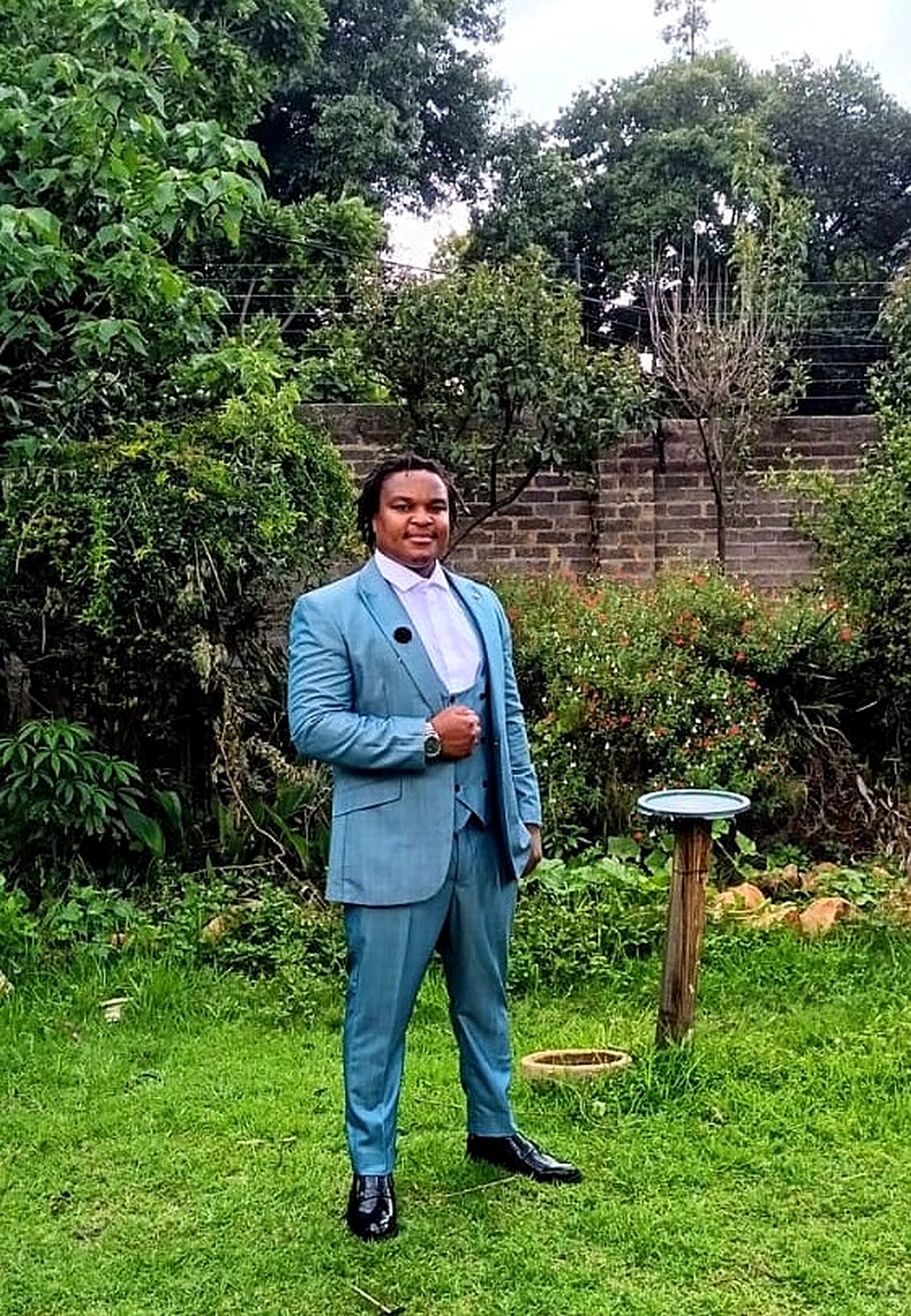 Anoshamisa Clive Benhura in a light blue suit, standing in a garden